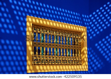 Yellow window with a grid on the background of two blue walls with sun reflections in Marrakesh, Morocco             