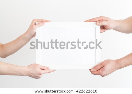 Hands of the man and the woman hold a frame with a clean sheet on a white background. White frame with a clean sheet on a white background.