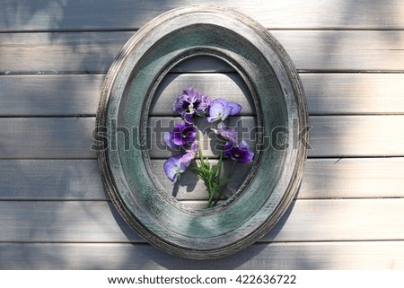 Fresh bouquet of purple and violet pansies in the green wooden oval frame on the grey background, warm and sunny spring day