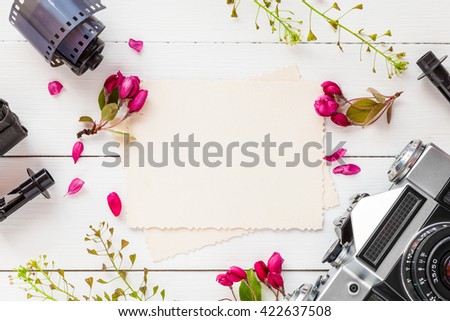Empty photo frame for the inside, retro camera, photo film rolls and apple flowers on white background. Flat lay, top view.
