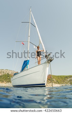 Young lady standing on the sail boat anchored in a calm blue water bay Royalty-Free Stock Photo #422650663