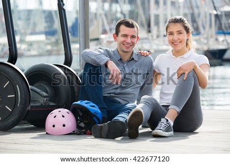 Happy young man and woman with the segways making photos against a yachts. Focus on both persons 