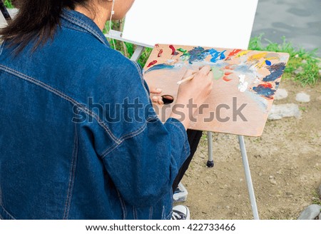 Young woman is painting near the river.