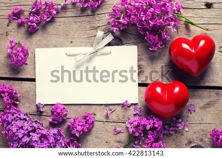 Fresh violet lilac flowers, decorative red hearts and empty tag on aged  wooden planks. Selective focus. Place for text. Toned image.
