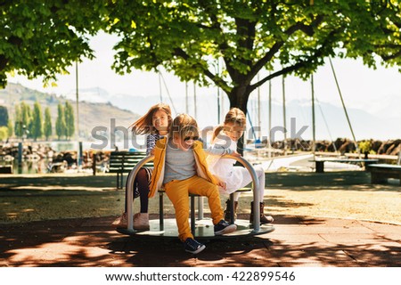 Three kids having fun on playground. Stylish kids playing on merry-go-round in the park on a very sunny day. Adorable children friends spending time together Royalty-Free Stock Photo #422899546
