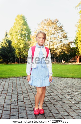 A young little girl preparing to walk to school, wearing blue mary jane dress and red moccasins