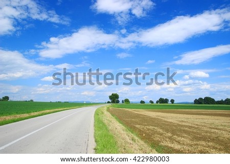 Beautiful landscape with road, agricultural fields and blue sky with some clouds 