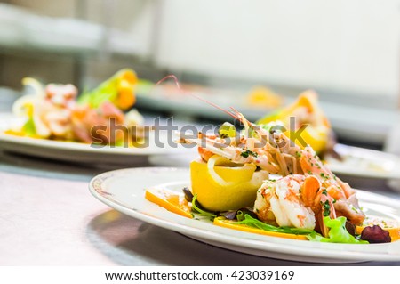 Delicious shrimp appetizer with colorful  fresh mediterranean fruits garnish on elegant white plates in restaurant kitchen Royalty-Free Stock Photo #423039169