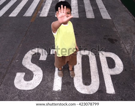 Photo of a Young boy makes a stop sign while standing on a word "stop" next to a pedestrian lane