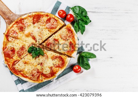 Hot true PEPPERONI ITALIAN PIZZA with salami and cheese. TOP VIEW Tasty traditional pepperoni pizza on board on white wooden table with decoration and slice. Copy space for logo. Ideal for commercial 