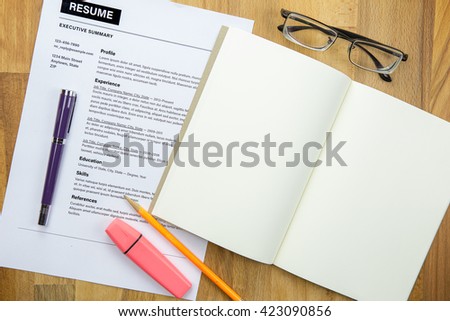 Top view of office desk with resume information, notebook, highlighter, pencil, pen and glasses.