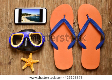 high-angle shot of a rustic wooden table full of summer stuff, such a pair of flip-flops, a diving mask, a starfish and a smartphone with the picture of a beach taken by myself in its screen