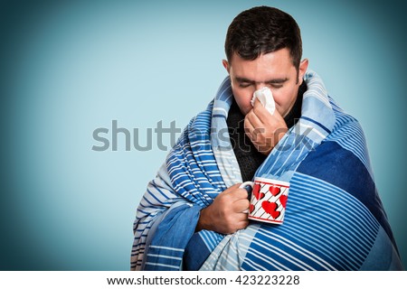 Portrait of a sick man with the flu, allergy, germs,cold, blowing his nose with tissue and holding a warm tea cup Royalty-Free Stock Photo #423223228