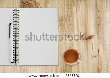 Blank notepad and coffee cup on wooden table.