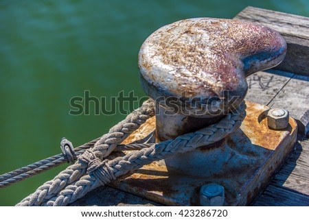Thick mooring rope around a large rusty iron cleat on a weathered old wooden jetty