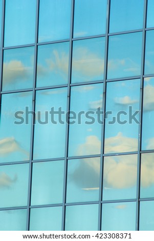 Vertical shot of clouds and blue sky reflected in modern office building windows.