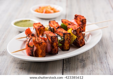 Paneer Tikka Kabab in red sauce - is an Indian dish made from chunks of cottage cheese marinated in spices & grilled in a tandoor. Served in a plate with salad & green mint chutney. Selective focus Royalty-Free Stock Photo #423385612