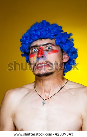 Close-up portrait. Clown in a blue wig, expressing surprise. Yellow background