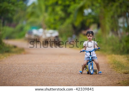 cute thai-indian girl riding her bike on a dirt road. focus on the girl with a shallow depth of field and lot of free space.