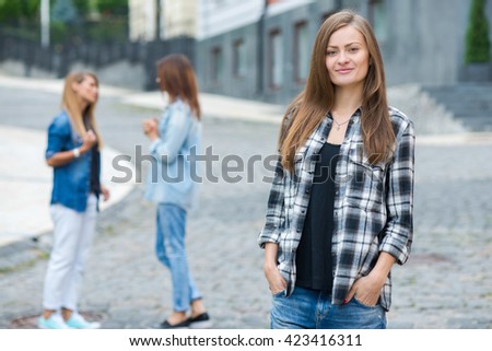 Street style stylish girl. Portrait of young and beautiful girl standing on the street. Her friends are behind her, having fun and good cheerful time