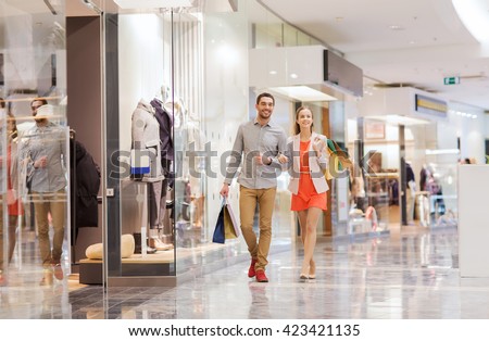 sale, consumerism and people concept - happy young couple with shopping bags walking in mall Royalty-Free Stock Photo #423421135