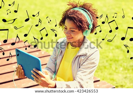 people, summer, technology and leisure concept - happy african american young woman in headphones with tablet pc computer listening to music or watching video outdoors over notes background