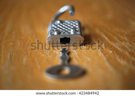Small metal key opening or closing an silver lock on the wooden surface 