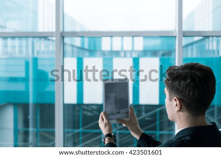 Young man doing a photo of modern building of college with new tablet