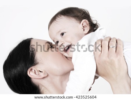 young beautiful mother holding and kissing her cute baby girl , studio shot with light background.