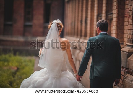 Happy newlywed couple holding hands near old castle wall