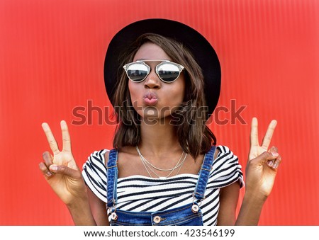 Beautiful smiling african woman in a black hat over colorful red background. Fashion portrait stylish woman in sunglasses outdoor.