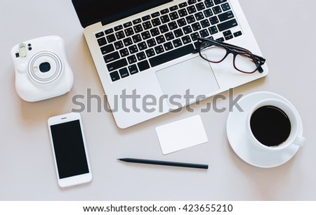Creative flat lay photo of workspace desk with laptop, blank paper, coffee, eyeglasses, smartphone and camera on grey background : clean and simplicity style
