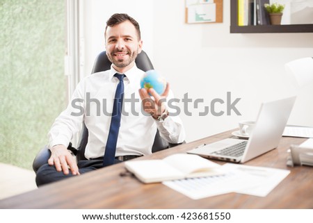 Portrait of a handsome young Latin man holding a small globe as a sign that he runs a global business