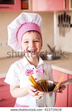  close-up portrait of little boy in the hat of the chef and an apron. Little cooks chef in the kitchen preparing spaghetti. Emotional pictures