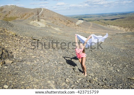 Photo of Teenager young adult gymnastics with white material. Cute sporty woman stand on stones floor against mountain perspective and blue sky with clouds on nature background landscape