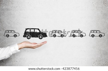 Man's hand choosing black car sketch over row of white cars on concrete wall. Concept of choice