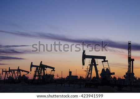 Pump jacks and derrick silhouette during sunset on the oilfield. Oil and gas concept. 