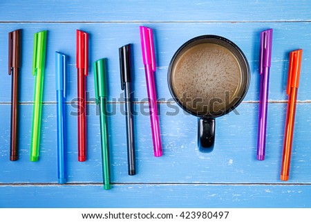 Coffee cup and color pen on the blue wooden background
