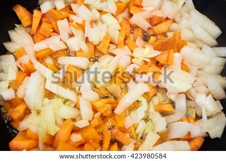 Closeup mixture of chopped carrots and onions in a frying pan fried in oil.