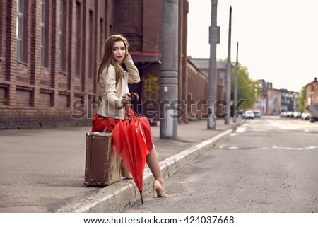 Portrait of a young woman sitting on an old suitcase with umbrella in the street
