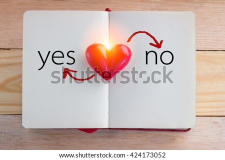 Book with opened pages and clay heart shape in the middle with word yes or no on wooden background : love concept