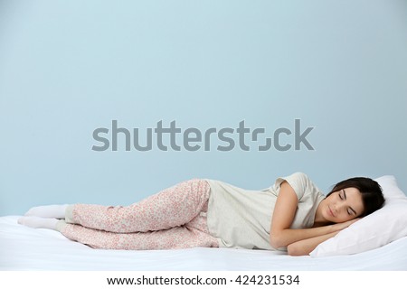 Young woman in pajamas sleeping on bed on blue background Royalty-Free Stock Photo #424231534