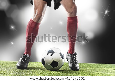 close up legs and feet of football player in red socks and black shoes running and dribbling with the ball playing on stadium pitch with background flashes and light flares
