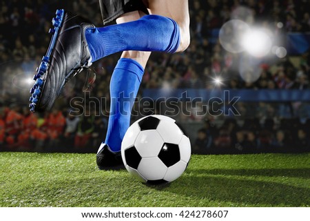 close up legs and feet of football player in action wearing blue socks and black shoes running and dribbling with the ball playing match on green grass pitch at  soccer stadium with flashes and flares