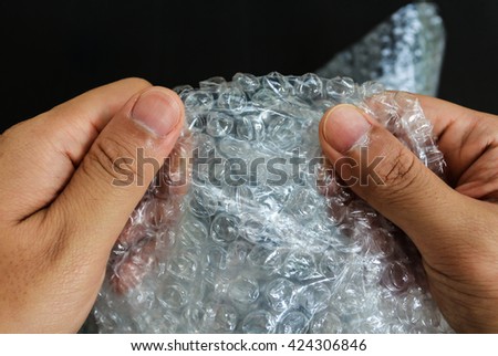 hands popping the bubbles in bubble wrap on black background (selective focus) Royalty-Free Stock Photo #424306846