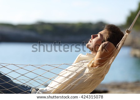 Side view of a casual happy man relaxing on a hammock in the beach on holidays Royalty-Free Stock Photo #424315078