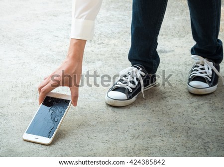 Person Picking Broken Smart Phone (Cracked Screen) of the Ground Royalty-Free Stock Photo #424385842
