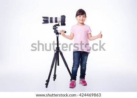 little cute girl holding a modern professional photo camera on tripod. child photographs