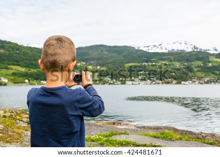 Young boy in Norway taking a picture of the surrounding scenery with his compact digital camera.