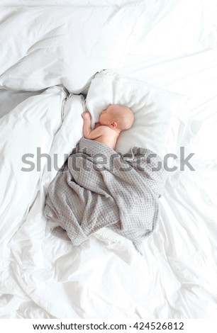 Newborn sleeping on white bed in grey blanket